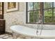 Close-up of a sleek tub with a vintage faucet and marble tiled walls under a window at 5902 E Arcadia Ln, Phoenix, AZ 85018