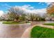 Community entrance with a circular flower bed, mature trees, and brick-paved driveway leading to a gated home at 20690 E Sunset Dr, Queen Creek, AZ 85142