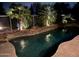 Stunning dark water pool with lush landscaping and stone accents, illuminated for a captivating evening ambiance at 6181 E Brilliant Sky Dr, Scottsdale, AZ 85266
