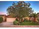 Inviting brick home featuring manicured lawn, large shade tree, lush landscape, and an attached two car garage at 4945 E Shapinsay Dr, San Tan Valley, AZ 85140