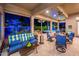 A covered outdoor living space features comfortable blue-cushioned seating and dining with a view of the pool at night at 19644 N Majestic Vista Ct, Surprise, AZ 85387