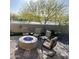 A cozy outdoor patio features a brick floor, comfortable seating around a modern fire pit, and lush green trees in the background at 5195 N 207Th Dr, Buckeye, AZ 85396