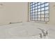 Close-up view of the soaking tub with a glass block window providing natural light in the bathroom at 16927 W Desert Blossom Way, Surprise, AZ 85387