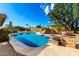 Backyard featuring a sparkling pool with natural stone surround, complemented by mature trees and desert landscaping at 7656 W Wagoner Rd, Glendale, AZ 85308