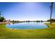Scenic view of a serene lake surrounded by lush green grass, landscaping, and waterfront homes at 1210 E Azure Sea Ln, Gilbert, AZ 85234
