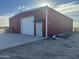 The red metal exterior of the industrial building featuring a single roll up door and a walk-in entrance at 9600 S 393Rd Ave, Tonopah, AZ 85354