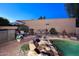 Poolside view featuring a rock waterfall, outdoor seating, and lush desert landscaping at 16857 E Deuce Ct, Fountain Hills, AZ 85268