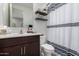 Cozy bathroom featuring a dark wood vanity, decorative shelves, and a modern striped shower curtain at 17454 W Red Fox Rd, Surprise, AZ 85387