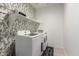 Convenient laundry room with modern washer and dryer, stylish wallpaper, and ample shelving at 17454 W Red Fox Rd, Surprise, AZ 85387