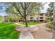 Exterior view of a condominium building, sidewalks, luscious grass, and a large shade tree in the community at 14950 W Mountain View Blvd # 5312, Surprise, AZ 85374