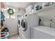 Bright laundry room featuring white washer, dryer, freezer, storage shelves, and a sunlit window with a wreath at 927 E Baylor Ln, Gilbert, AZ 85296