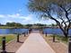 Waterfront view of the pond from a cemented walkway, lined with trees and lamp posts at 37083 W Prado St, Maricopa, AZ 85138