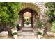 Inviting stone entryway with arched opening and lush landscaping, offering a glimpse of the outdoor dining area at 10040 E Happy Valley Rd # 269, Scottsdale, AZ 85255