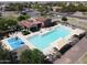Aerial view of a clean community pool with lounge chairs, splash pad and picnic space, all bordered by green trees at 19072 N Ventana Ln, Maricopa, AZ 85138