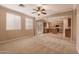 Open-concept living room with neutral tones, large windows, ceiling fan, and direct access to the kitchen area at 19072 N Ventana Ln, Maricopa, AZ 85138
