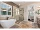 Luxurious bathroom with a modern freestanding tub, a glass-enclosed shower, and neutral tile at 7589 W Firebird Dr, Glendale, AZ 85308