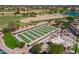 Aerial view of community bocce ball courts and lush green golf course featuring mature trees and sand traps at 15696 W Roanoke Ave, Goodyear, AZ 85395