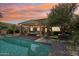 A backyard scene with a view of the pool, patio with a fire pit, and lush landscaping under a colorful sunset at 18504 W Maui Ln, Surprise, AZ 85388