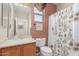 Cozy bathroom with wood cabinets, a shower with patterned curtain, and picture window at 26288 W Horsham Ct, Buckeye, AZ 85396