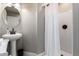 Cozy bathroom features a sleek pedestal sink, a round mirror and a shower with a white shower curtain at 2644 E Sylvia St, Phoenix, AZ 85032