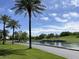 This view of the golf course features a pond, lush greenery, and palm trees under a partly cloudy sky at 26735 N 127Th Dr, Peoria, AZ 85383