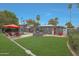 Expansive backyard featuring a pool, patio with red umbrella, lush lawn, and modern gray house at 6746 E Monterosa St, Scottsdale, AZ 85251