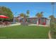 Expansive backyard featuring a pool, patio with red umbrella, lush lawn, and modern gray house at 6746 E Monterosa St, Scottsdale, AZ 85251