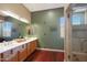 Bathroom featuring double sinks, a large mirror, beautiful hardwood floors and a glass shower door at 14442 W Lexington Ave, Goodyear, AZ 85395