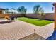 Brick backyard patio featuring green lawn, outdoor seating, and lush desert landscaping at 2185 N Beverly Pl, Buckeye, AZ 85396