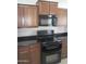 Modern kitchen showing black appliances, wooden cabinetry, and granite countertops for a practical, stylish cooking area at 37180 W Mondragone Ln, Maricopa, AZ 85138