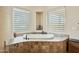 A luxurious soaking tub surrounded by travertine tile and natural light from two windows at 40627 N 6Th Ave, Phoenix, AZ 85086