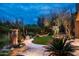 A serene desert backyard oasis features lush greenery, accent lighting, a fountain, and travertine patio at 9722 E Mark Ln, Scottsdale, AZ 85262