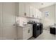 Bright laundry room with cabinets, sink, black washer and dryer, and white door at 21387 W Meadowbrook Ave, Buckeye, AZ 85396