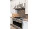 A close-up view of the kitchen with a stainless steel stove, hood, white cabinets, and beautiful tile backsplash at 23434 N 76Th Way, Scottsdale, AZ 85255