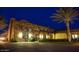 Elegant exterior of a community clubhouse featuring stone accents, porte cochere, and lush landscaping at night at 36053 N Stoneware Dr, Queen Creek, AZ 85140