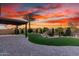 Enjoy this property's backyard that has a paved patio, a tall palm tree and an abundance of desert trees under a fiery sunset at 21647 S 223Rd Pl, Queen Creek, AZ 85142
