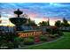 Elegant community entrance featuring a water fountain, lush landscaping, and a picturesque sunset at 12860 W Junipero Dr, Sun City West, AZ 85375