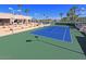 Well-maintained tennis court with bright blue and green surface, surrounded by lush greenery and palm trees at 25273 S Berry Brook Dr, Sun Lakes, AZ 85248