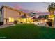 Expansive backyard boasts lush artificial turf, a covered patio, a BBQ, and a sparkling pool at dusk at 69 E Benrich Dr, Gilbert, AZ 85295