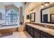 Bright bathroom with double sinks, stone countertops, a soaking tub under a large window and tiled floors at 17246 N 56Th Way, Scottsdale, AZ 85254