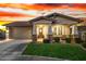 Charming single-story home with a well-manicured lawn and inviting front porch, illuminated by a colorful sunset at 11366 W Ashby Dr, Peoria, AZ 85383