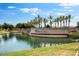 A scenic community entrance showcases a tranquil lake, lush palm trees, and a welcoming Ajante sign at 16749 W Whispering Wind Dr, Surprise, AZ 85387