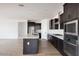 Open concept kitchen features dark cabinets, an island, stainless steel appliances, and tile backsplash at 16749 W Whispering Wind Dr, Surprise, AZ 85387