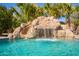 Close-up of a rock waterfall feature cascading into a sparkling pool, surrounded by lush greenery at 21256 E Waverly Dr, Queen Creek, AZ 85142