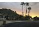 Desert community entrance featuring lush landscaping with cacti and palm trees, set against a mountain backdrop at sunset at 2233 E Behrend Dr # 85, Phoenix, AZ 85024