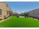 Lush backyard featuring an artificial grass lawn, paved patio area with seating, and colorful potted plants at 2424 S 235Th Dr, Buckeye, AZ 85326
