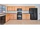Functional kitchen featuring wood cabinetry, black appliances, and tiled flooring for easy maintenance at 44917 W Zion Rd, Maricopa, AZ 85139