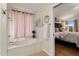 Bright bathroom featuring a corner soaking tub, pink curtains, and an open doorway to the bedroom at 5471 W Quail Ave, Glendale, AZ 85308