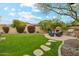 Lush backyard featuring a stone fireplace, built-in grill, and manicured lawn surrounded by mature trees at 17727 N 95Th Pl, Scottsdale, AZ 85255