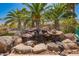 Charming rock water feature cascading into a koi pond set amid lush landscaping and mature palm trees in the backyard at 18867 N Cactus Flower Way, Surprise, AZ 85387